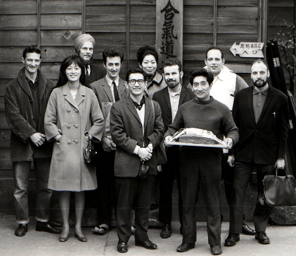 The foreign students about to deliver his birthday cake to O Sensei. From left to right: Norman Miles, Joanne Willard, Per Winter, Alan Ruddock, a visitor from the U.S., Joanne Shimamoto, Joe Deisher, Henry Kono, Terry Dobson, and Ken Cottier.